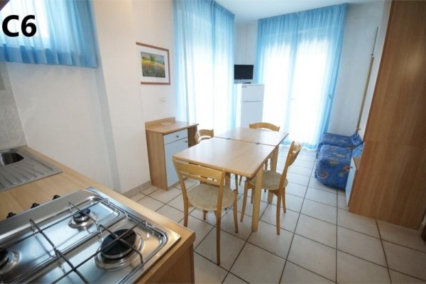 Kuchnia z jadalnianym stołem i krzesłami, obok której znajduje się sofa i okno z niebieskimi zasłonami.