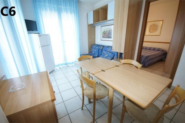 Widok na jasny pokój z stołem jadalnym, krzesłami, sofą i lodówką.