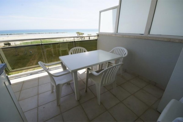 Balkon z widokiem na plażę i morze, wyposażony w cztery białe plastikowe krzesła i stół.