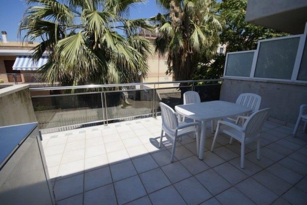 Słoneczny taras z białymi plastikowymi meblami i palmami w tle.