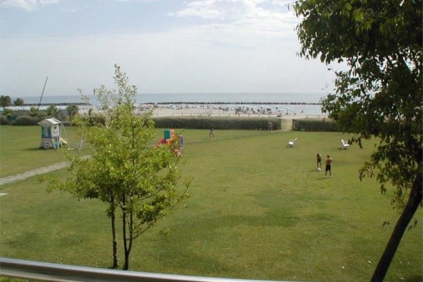 Nadmorska plaża z ludźmi i zielonym trawnikiem na pierwszym planie.