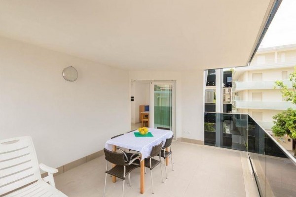 Przestronny balkon ze stołem jadalnym i krzesłami obok przeszklonej balustrady, widok na okoliczny budynek i drzewa.