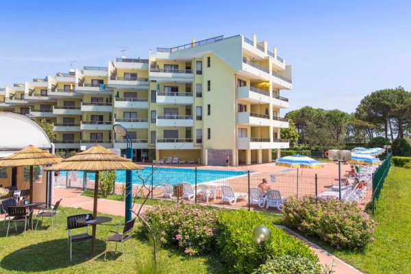 Budynek z apartamentami obok odkrytego basenu otoczonego leżakami i parasolami.