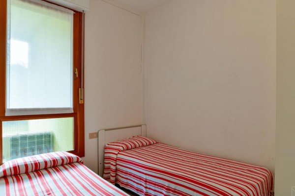 Dwa pojedyncze łóżka z czerwono-białą pasiastą pościelą w prostym pokoju z oknem.