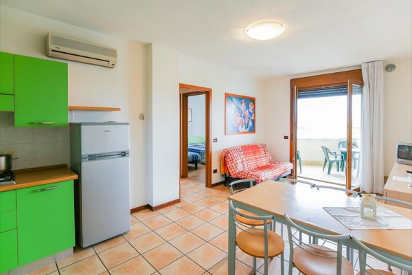 Nowoczesny salon z kuchnią w zielonych kolorach, sofą i wyjściem na balkon.
