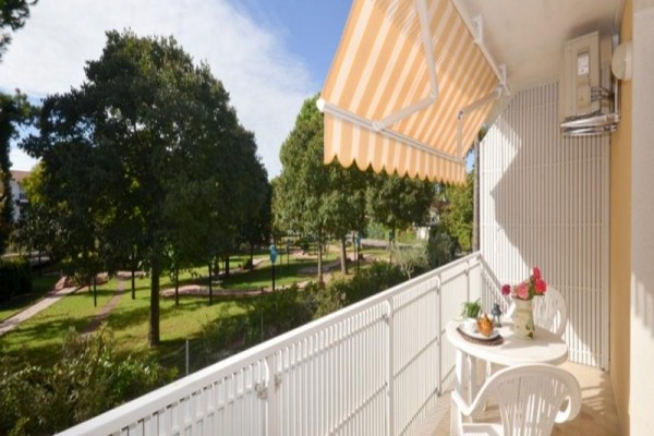 Balkon z plastikowymi meblami i markizą z widokiem na zielony park.