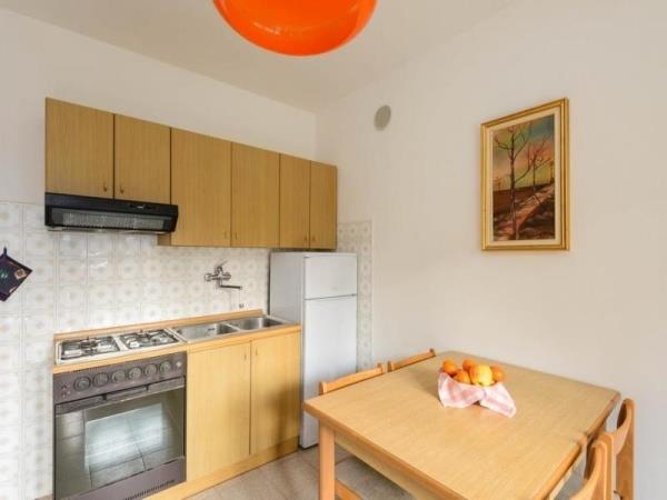 Mała kuchnia z kuchenką gazową, lodówką, stołem i miską owoców na stole.