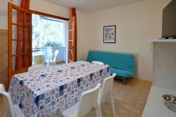 Pomieszczenie mieszkalne z jadalnianym stołem, krzesłami, rozkładaną sofą i otwartymi drzwiami na balkon.