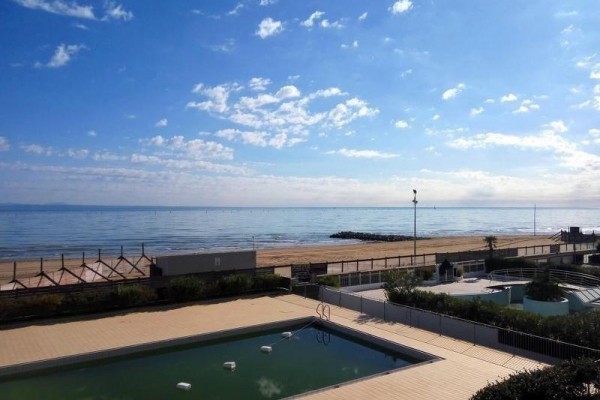 Widok na basen, plażę i spokojne morze w słoneczny dzień.