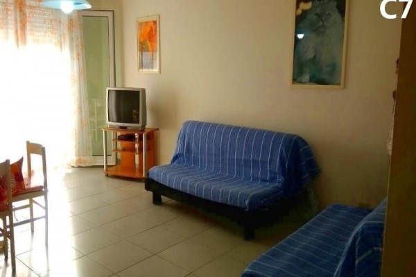 Salon z niebieską sofą, starszym telewizorem i obrazami na ścianach.