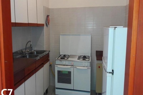 Mała kuchnia z kuchenką gazową, zlewem i lodówką.