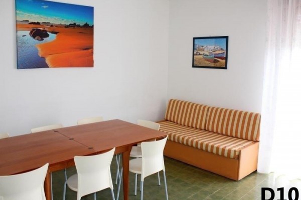 Jadalnia z drewnianym stołem, białymi krzesłami, pomarańczową kanapą i dwoma obrazami na ścianie.