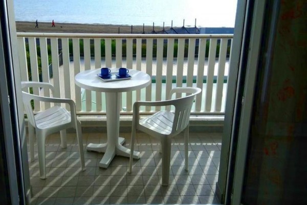 Balkon z plastikowym stolikiem, dwoma krzesłami i widokiem na morze.