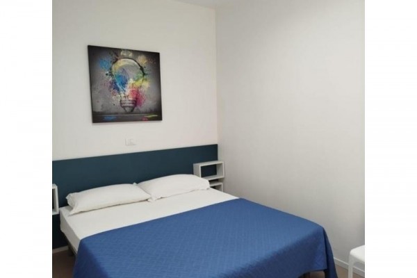 Otworzone drzwi prowadzące z pokoju na balkon z widokiem na drzewo.