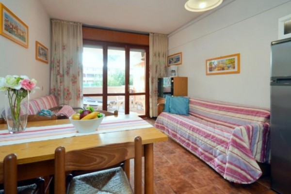 Salon z stołem jadalnym, kanapą, kwiatami na stole i widokiem na balkon.